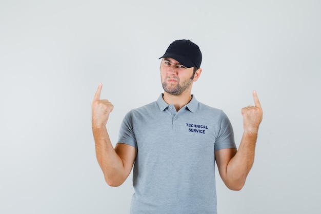 Young technician pointing up in grey uniform and looking hesitant.