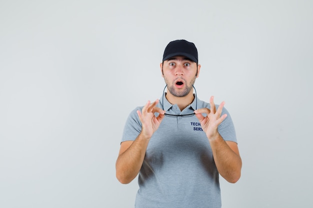 Free photo young technician taking off glasses in grey uniform and looking surprised.