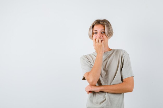 Young teen boy biting nails emotionally in t-shirt and looking anxious. front view.