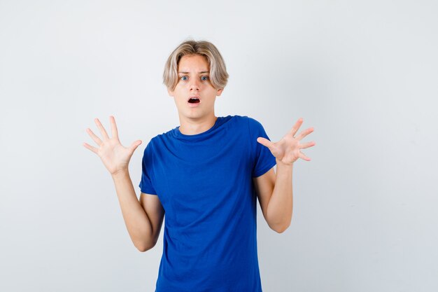 Young teen boy in blue t-shirt showing surrender gesture and looking frightened , front view.