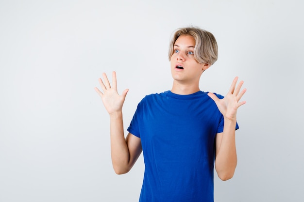 Young teen boy in blue t-shirt showing surrender gesture and looking frightened , front view.