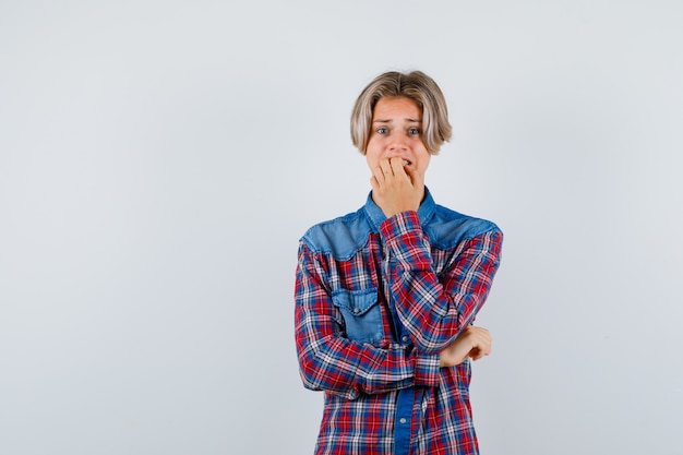 Young teen boy in checked shirt biting nails emotionally and looking anxious