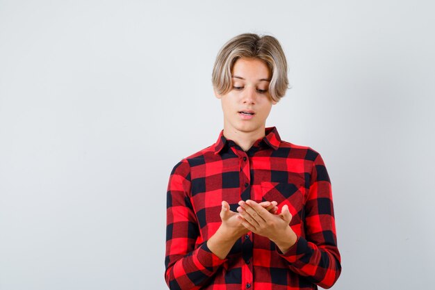 Free photo young teen boy in checked shirt looking at his palm and looking thoughtful , front view.