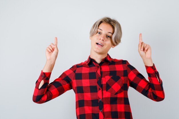 Young teen boy in checked shirt pointing up and looking cheery , front view.