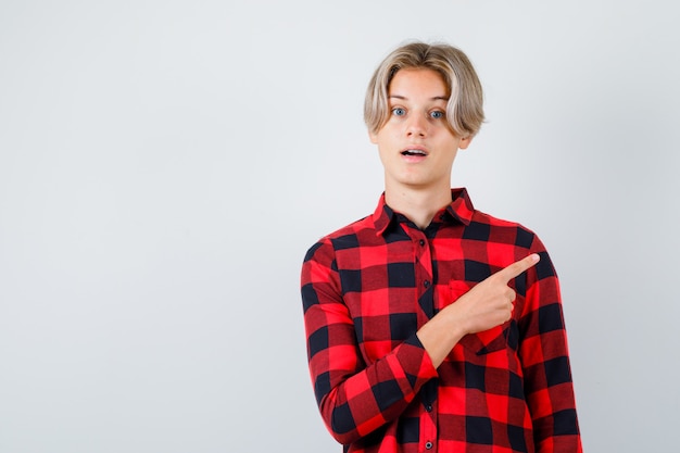 Young teen boy in checked shirt pointing at upper right corner and looking wondered , front view.
