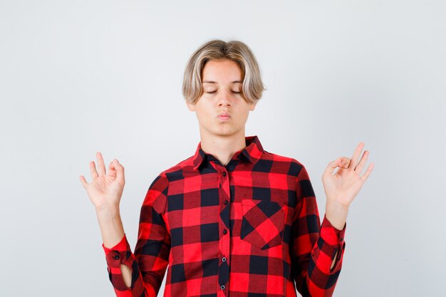 Young teen boy in checked shirt showing meditation gesture and looking relaxed , front view.