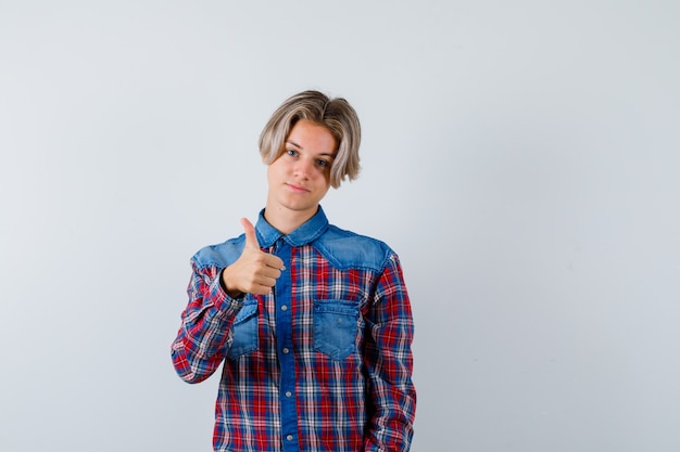 Young teen boy in checked shirt showing thumb up and looking pleased , front view.