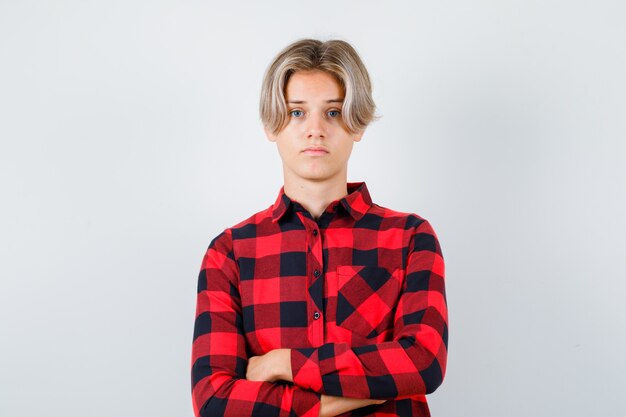 Young teen boy in checked shirt with hands crossed and looking confident , front view.