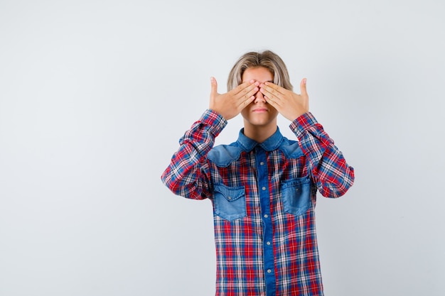 Free photo young teen boy covering eyes with hands in checked shirt and looking scared