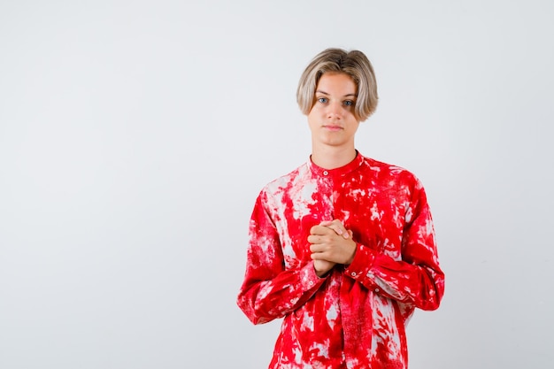 Young teen boy holding clasped hands over chest in shirt and looking confident , front view.