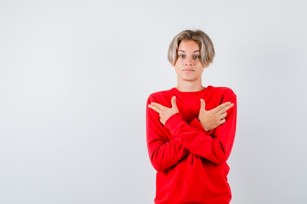 銃のジェスチャーを示し、優柔不断に見える赤いセーターを着た若い十代の少年、正面図。 Premium写真