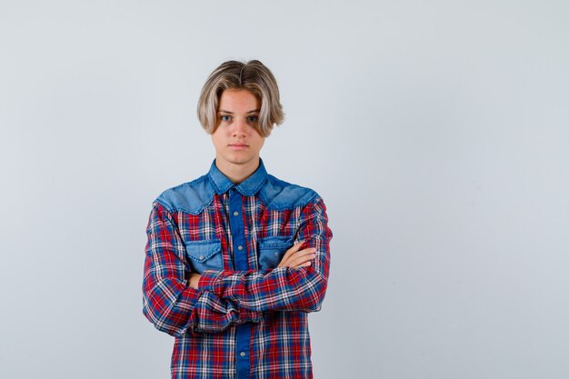 Young teen boy keeping arms folded in checked shirt and looking serious. front view.