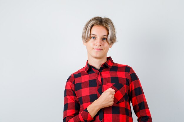 Young teen boy keeping fist over chest in checked shirt and looking confident , front view.