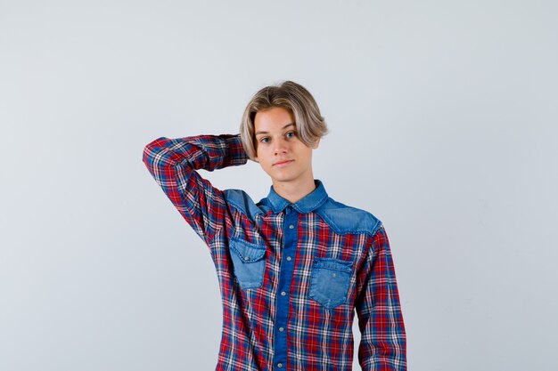 Young teen boy keeping hand behind head in checked shirt and looking confident. front view.