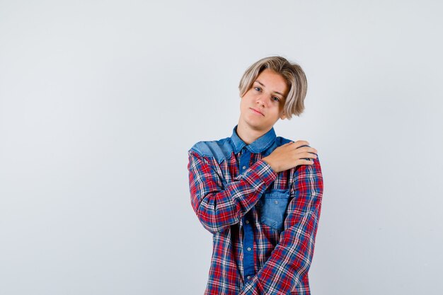 Young teen boy keeping hand on shoulder in checked shirt and looking upset , front view.