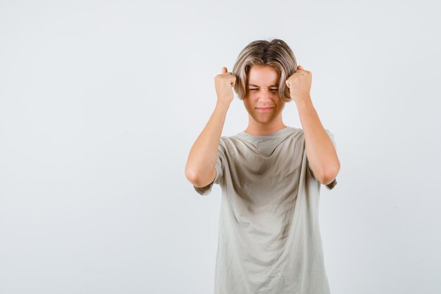 Young teen boy keeping raised fists near head in t-shirt and looking forgetful. front view.