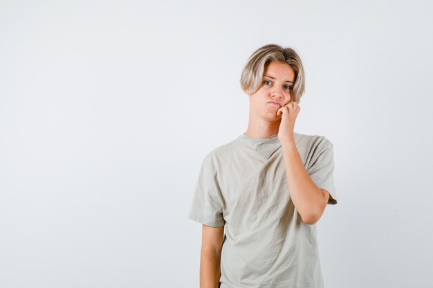 Young teen boy leaning cheek on hand in t-shirt and looking disappointed. front view.