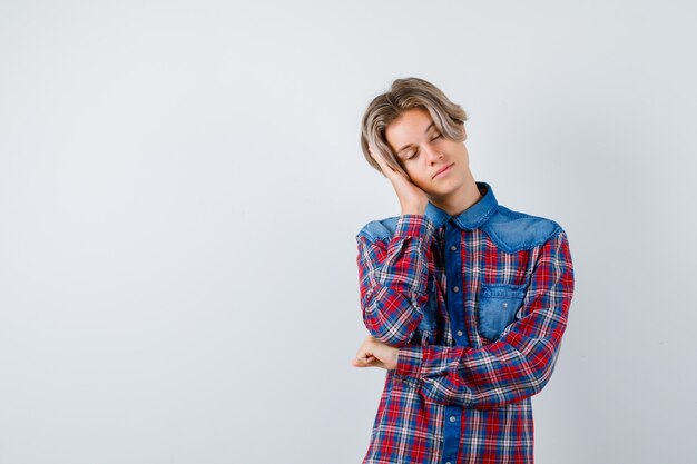 Young teen boy leaning on palm as pillow in checked shirt and looking tired , front view.