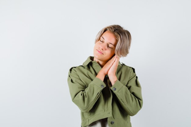 Young teen boy leaning on palms as pillow in green jacket and looking relaxed. front view.