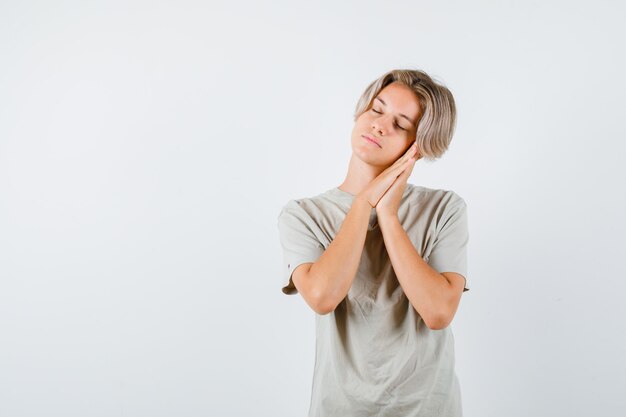 Young teen boy leaning on palms as pillow in t-shirt and looking sleepy. front view.