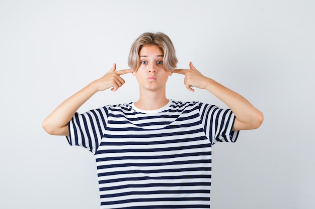 Young teen boy plugging ears with fingers, pouting lips in striped t-shirt and looking scared. front view.