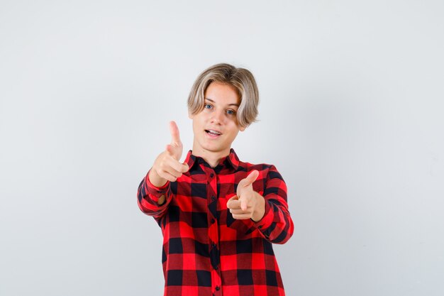 Young teen boy pointing at front in checked shirt and looking confident. front view.