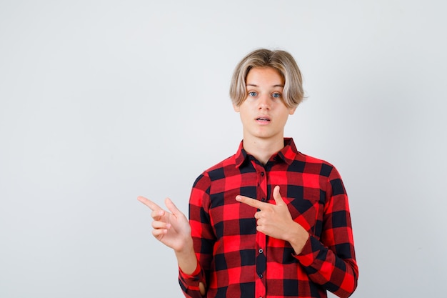 Foto gratuita giovane ragazzo adolescente che punta a sinistra in camicia a quadri e sembra perplesso, vista frontale.