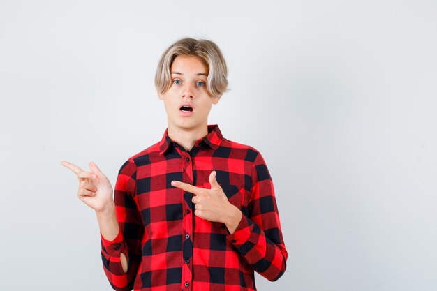 Young teen boy pointing to the left side in checked shirt and looking shocked , front view.