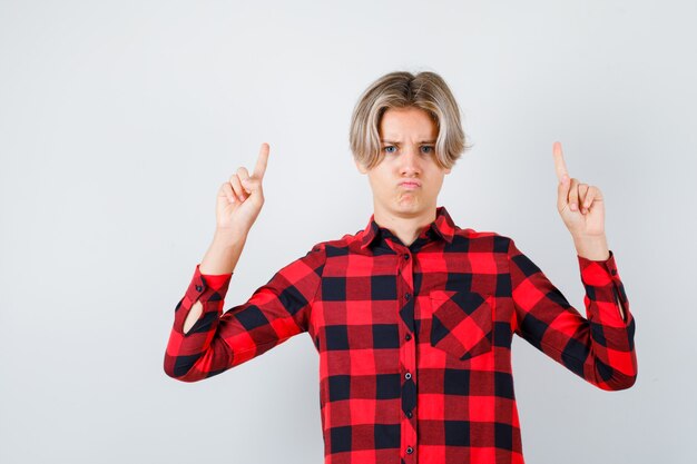 Young teen boy pointing up in checked shirt and looking disappointed , front view.