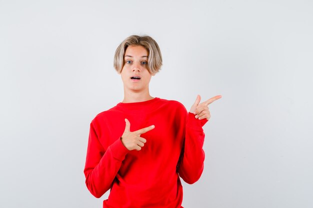 Young teen boy pointing at upper right corner in red sweater and looking puzzled. front view.