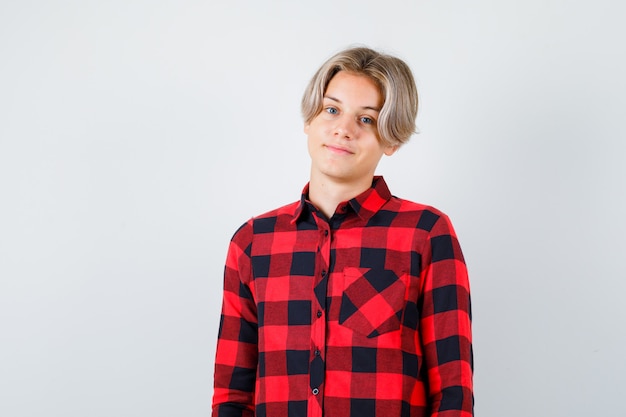 Young teen boy posing while standing in checked shirt and looking confident , front view.