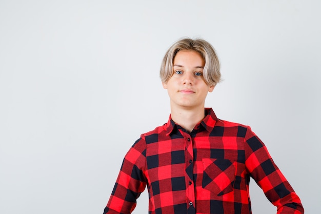 Young teen boy posing while standing in checked shirt and looking pleased . front view.