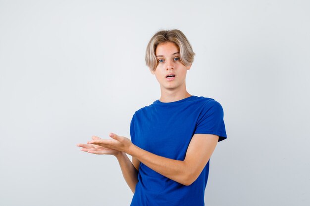Young teen boy pretending to show something in blue t-shirt and looking puzzled. front view.