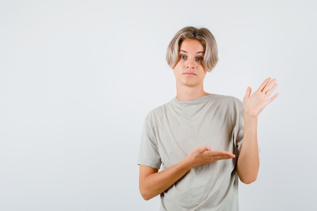 Tシャツで何かを見せているふりをして困惑しているように見える若い10代の少年。正面図。