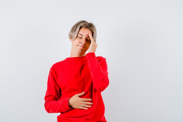 Young teen boy in red sweater feeling headache and looking tired , front view.