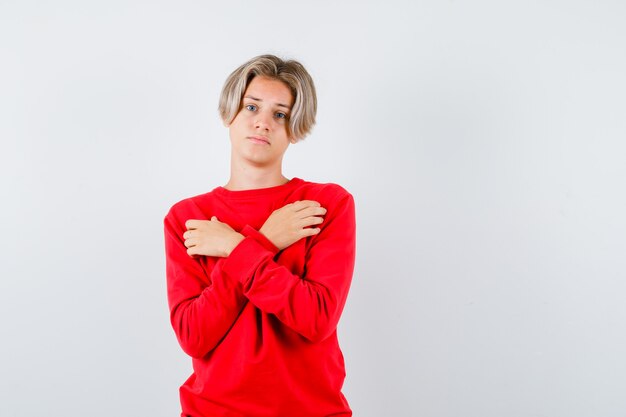 Young teen boy in red sweater holding crossed arms on chest and looking dismal , front view.