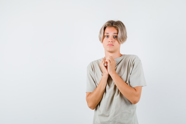 Young teen boy showing clasped hands in pleading gesture in t-shirt and looking disappointed. front view.