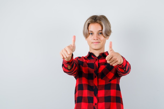 Foto gratuita giovane ragazzo adolescente che mostra il doppio pollice in alto in camicia a quadri e sembra allegro, vista frontale.