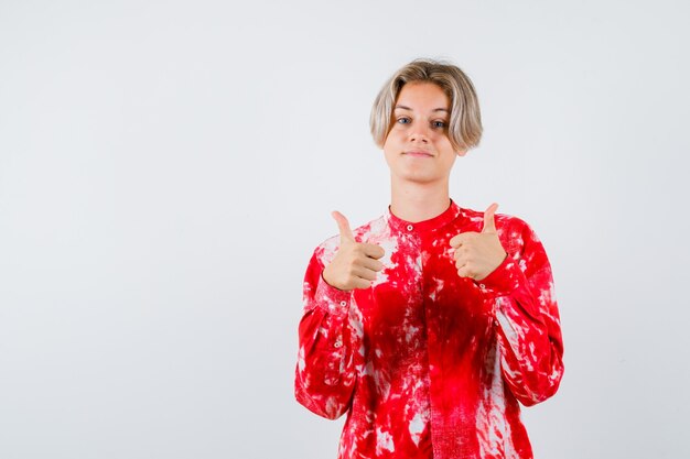 Young teen boy showing double thumbs up in shirt and looking confident , front view.