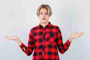 Free photo young teen boy showing helpless gesture in checked shirt and looking hesitant. front view.