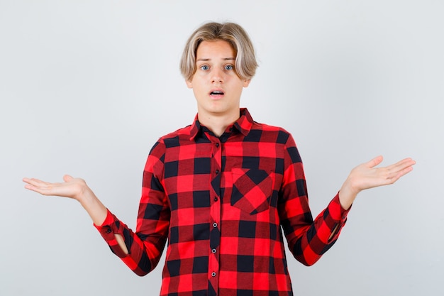 Бесплатное фото Молодой мальчик-подросток демонстрирует беспомощный жест в клетчатой рубашке и выглядит нерешительно. передний план.