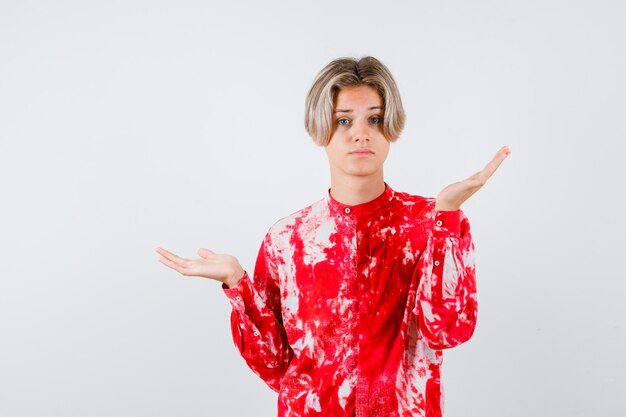 Young teen boy showing helpless gesture in shirt and looking confused , front view.