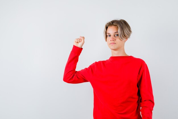 Young teen boy showing muscles of arm in red sweater and looking confident. front view.