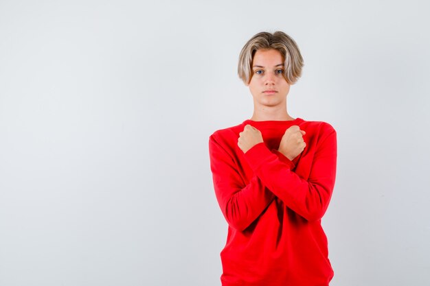 Молодой подросток мальчик показывает жест протеста в красном свитере и выглядит уверенно. передний план.