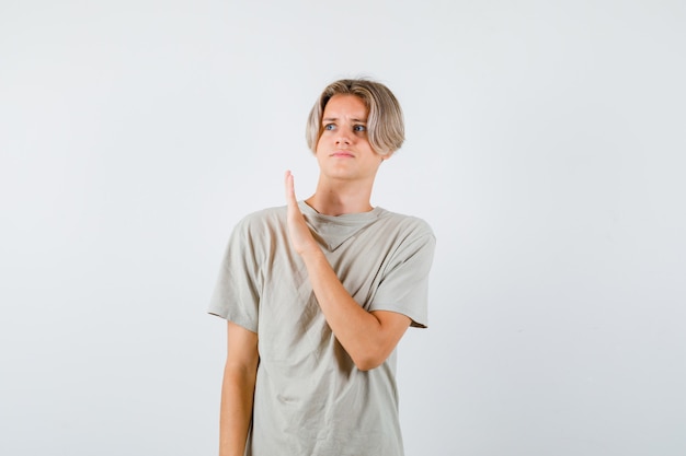 Young teen boy showing stop gesture while looking away in t-shirt and looking scared , front view.