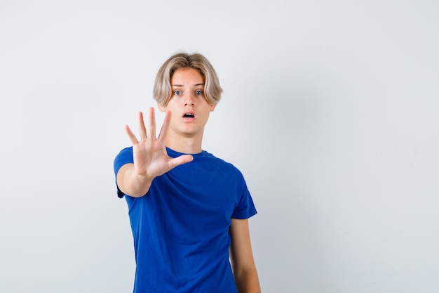 Free photo young teen boy showing stop sign in blue t-shirt and looking terrified , front view.