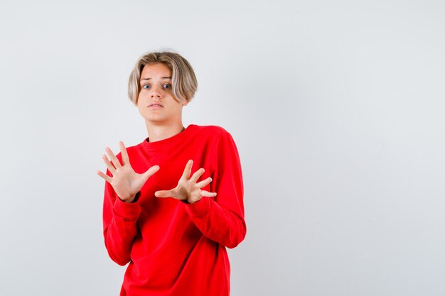 Young teen boy showing surrender gesture in red sweater and looking frightened. front view.
