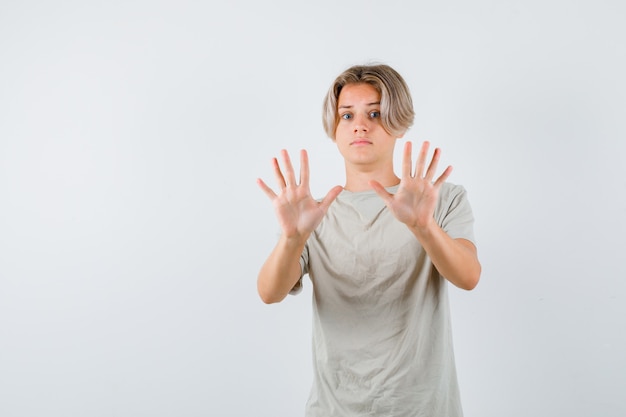 Young teen boy showing surrender gesture in t-shirt and looking frightened , front view.