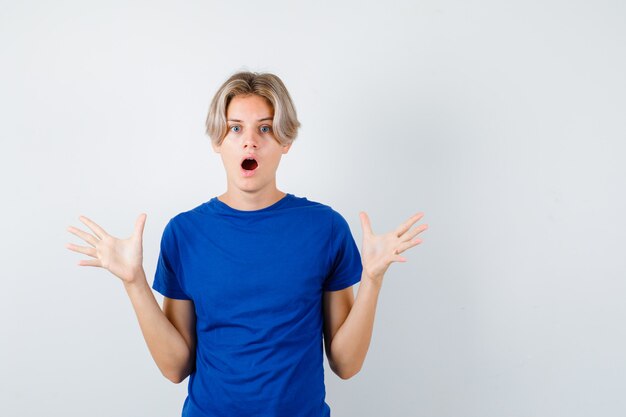 Young teen boy spreading palms out in blue t-shirt and looking shocked. front view.