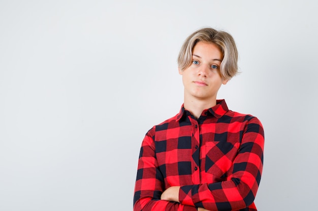 Young teen boy standing with crossed arms in checked shirt and looking confident , front view.